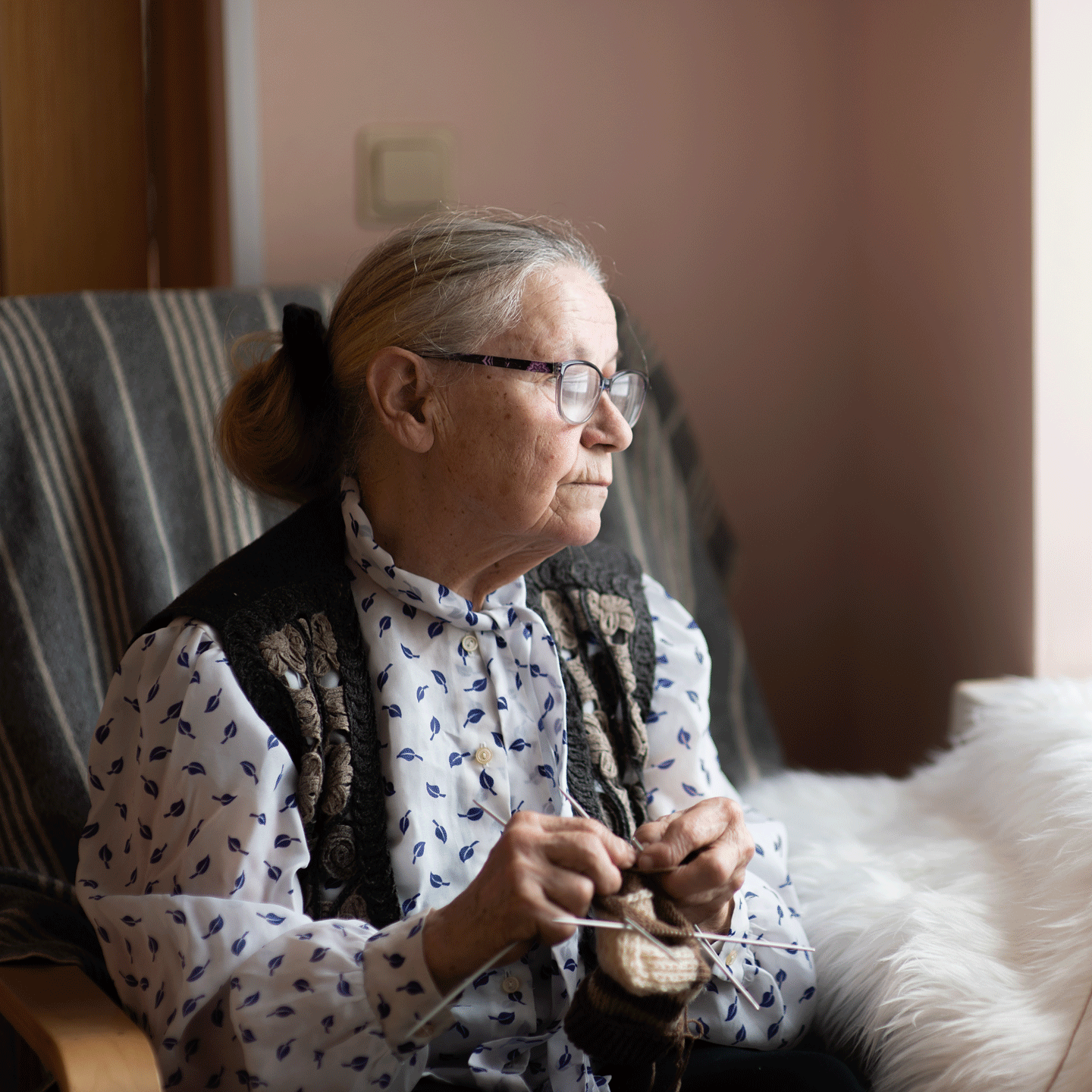 Señora de la tercera edad tejiendo mientras mira hacia una ventana.